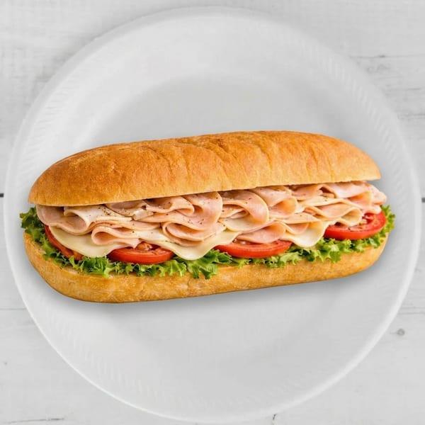 A turkey and cheese sub sandwich with lettuce and tomatoes on a white plate.