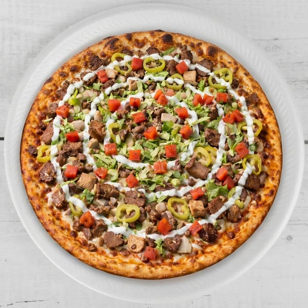 A round pizza topped with meat, diced tomatoes, green peppers, lettuce, and white sauce swirls.